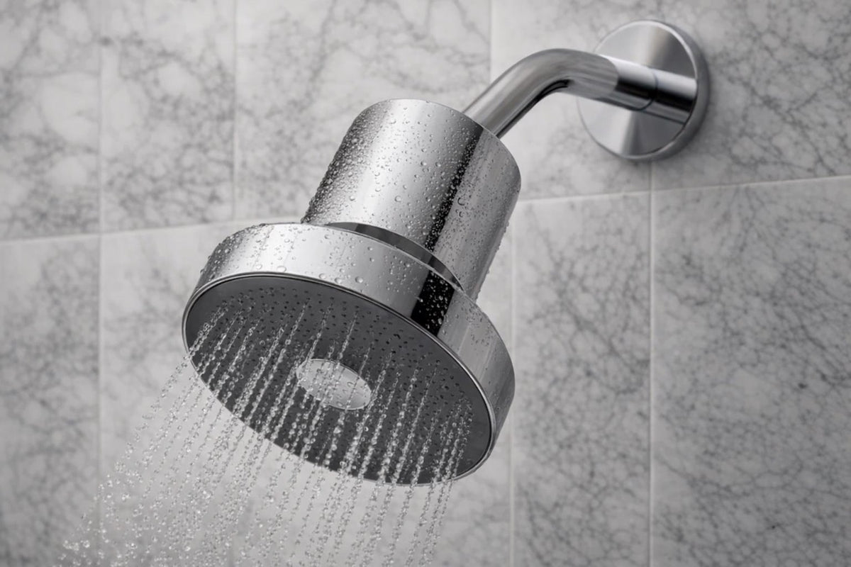 A polished chrome shower head mounted on a wall, shown with water spraying from the shower head against a gray marble-tiled background.
