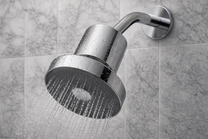 A polished chrome shower head mounted on a wall, shown with water spraying from the shower head against a gray marble-tiled background.