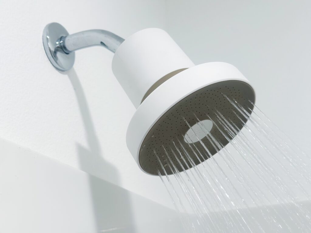 A modern white rain shower head mounted on a chrome wall arm, shown spraying water against a clean white wall.